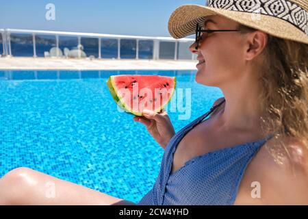 woman with slice of watermelon in straw hat sunbathing near swimming pool Stock Photo