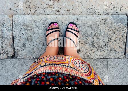 woman's feet in first person view with fuchsia painted nails and black shoes, in Moroccan tribal dress, on gray stone tiles. ethnicity concept Stock Photo