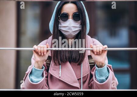 Female in medical mask outdoors behind the gate. Health protection and prevention of virus, coronavirus, COVID-19, epidemic and pandemic, infectious d