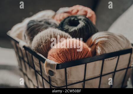 Close up of balls of earth coloured yarn inside a basket, sunlight from the window on it, selective focus. Stock Photo