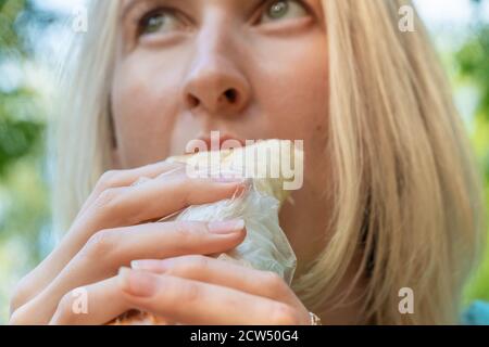 The girl the blonde eats shawarma on the street close up, focus on shawarma. Fast food, fast food. Stock Photo