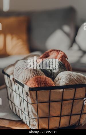 Balls of earth coloured yarn inside a basket on a table inside an apartment, sunlight from the window on it, selective focus. Stock Photo