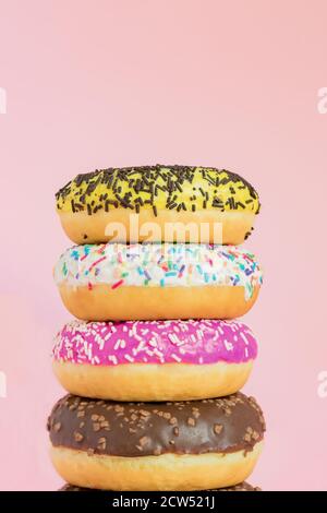Stack of glazed sweet doughnuts with sprinkles and nuts on pink background. Copy pace for your text Stock Photo