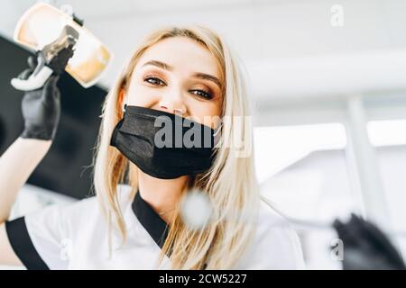 Portrait of young blond female dentist, wearing black mask and gloves. Woman looking at camera. Dentistry. Stock Photo