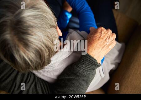 Close Up Rear View Of Loving Senior Couple At Home Hugging On Sofa Together