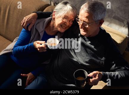 Loving Senior Couple Relaxing And Chatting On Sofa At Home Together With Hot Drink Stock Photo