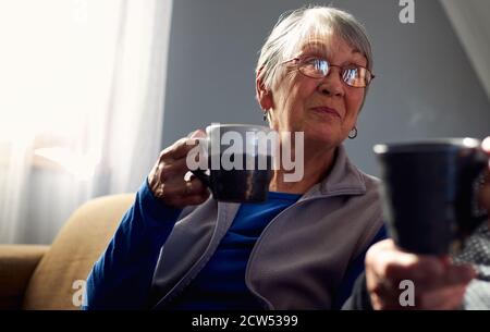Senior Couple Relaxing And Chatting On Sofa At Home Together With Hot Drink Stock Photo