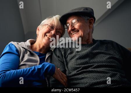 Laughing Senior Couple Sitting On Sofa At Home Watching Television Together Stock Photo