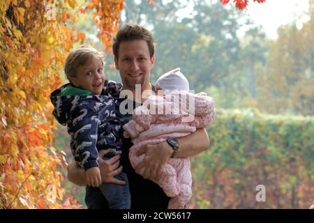 Autumn family walk in forest. Beautiful park with dry yellow and red leaves. Loving Father hugs daughter and son Stock Photo