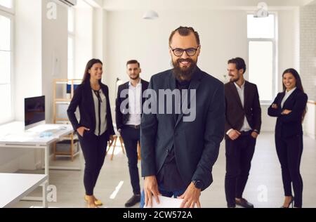 Cheerful young businessman with group of employees smiling and looking at camera Stock Photo