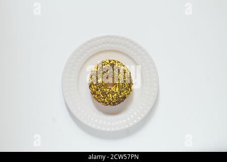 Glazed vanila and banana donuts with sprinkles on a plate on black stone background. Minimal flat lay with copy space Stock Photo