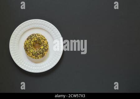 Glazed vanila and banana donuts with sprinkles on a plate on black stone background. Minimal flat lay with copy space Stock Photo