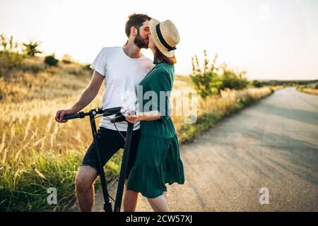 Portrait of young couple kissing on the background of natural landscape. Walking on electric scooters in the countryside. Stock Photo