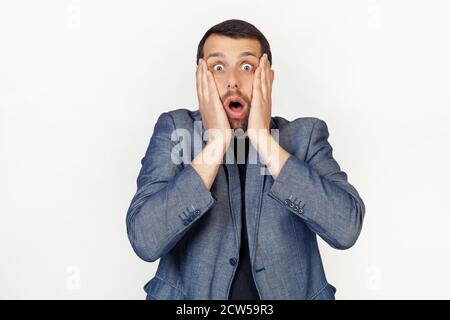 Young businessman man with a beard scared and shocked, surprised and surprised with hands on his face. Portrait of a man on a gray background. Stock Photo