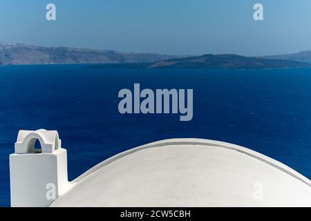 White roof with chimney on the Caldera at Oia, Santorini island, Greece. beautiful blue seascape with volcano in the background Stock Photo