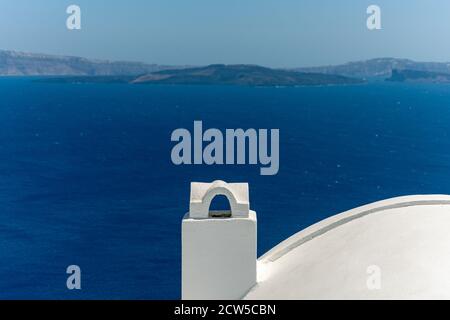 White roof with chimney on the Caldera at Oia, Santorini island, Greece. beautiful blue seascape with volcano in the background Stock Photo