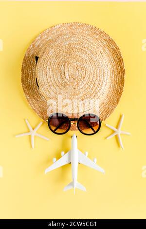Tourist face made of straw hat, model plane, airplane and sunglasses on yellow background. Traveler accessories concept.  Stock Photo
