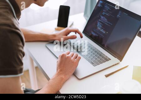 Young man mobile developer, programmer writes program code on a laptop Stock Photo