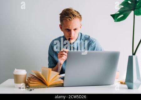 Focused caucasian man college student studying with books and laptop distantly Stock Photo