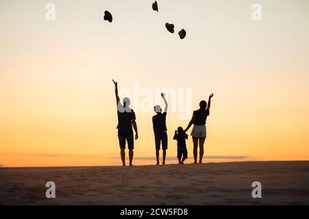 Silhouette of a family at sunset on the Sands. Mom and dad and two sons throw up their hats. Stock Photo