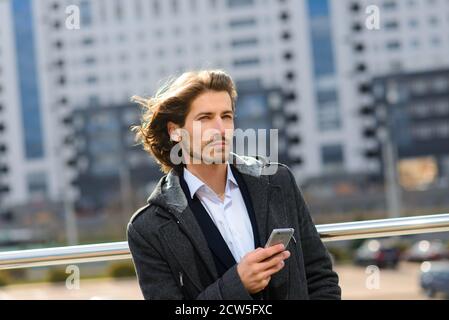 Modern confident young businessman in full suit stands outdoors with cityscape in the background Stock Photo