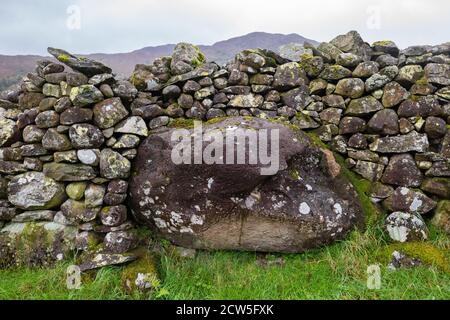 Dry stone wall built around and over a large erratic boulder - Lake District, England, UK Stock Photo