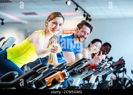 Woman showing thumbs up sign exercising of fitness bike in gym Stock Photo