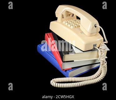 retro yellow telephone on stack of hardcover books isolated on black Stock Photo