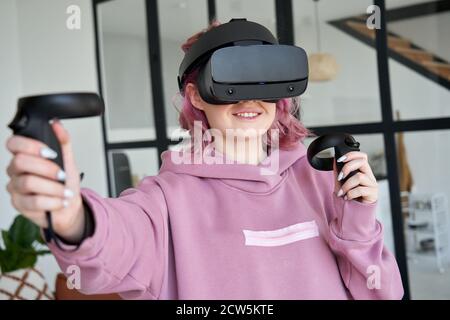 Woman gamer wear vr headset hold controllers play virtual reality game. Stock Photo
