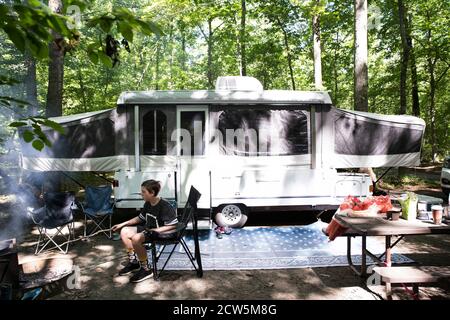 Tween Boy Roasts Hot Dog on a Stick, Sitting in Front of Pop Up Camper Stock Photo
