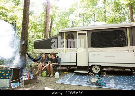 Wide View of Siblings Roasting Hot Dog Sitting in Front of Tent Camper Stock Photo