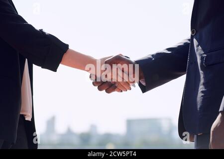 Handshake of young intercultural business partners in formalwear outdoors Stock Photo
