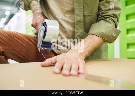 Close up of unrecognizable man sealing cardboard boxes with scotch tape gun while packing in self storage unit, copy space Stock Photo