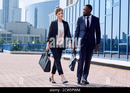 Young intercultural business partners in formalwear moving down sidewalk Stock Photo