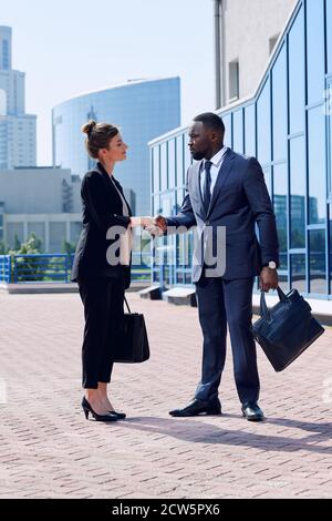Young successful intercultural business partners in formalwear shaking hands Stock Photo