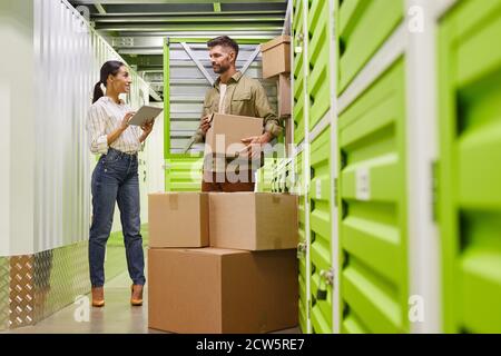 Full length portrait of modern couple using digital tablet while loading boxes into self storage container, copy space Stock Photo