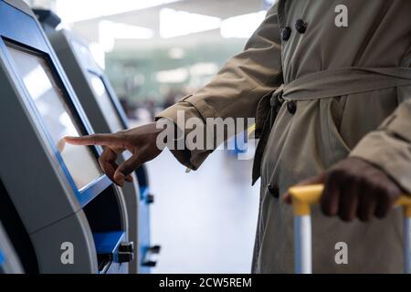 Black traveler man using self check-in machine kiosk service at airport, finger point on display. Close up. Stock Photo