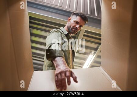 Low angle POV shot at handsome bearded man carrying box while loading self storage unit, copy space Stock Photo