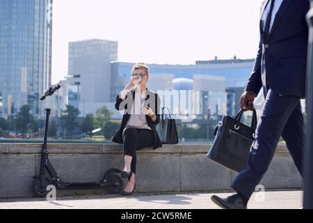 Young relaxed businesswoman scrolling in smartphone and drinking coffee Stock Photo