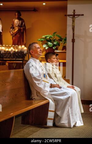 A robed deacon and two altar boys listen happily to the sermon during mass in a Southern California Catholic church. Stock Photo