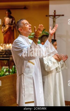 A robed deacon sings along with two altar boys as they participate in the mass at a Southern California Catholic church. Stock Photo