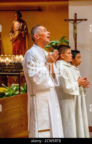A robed deacon sings along with two altar boys as they participate in the mass at a Southern California Catholic church. Stock Photo