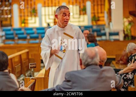 A robed deacon socializes with parishioners in pews before a wedding at a Southern California Catholic church. Stock Photo
