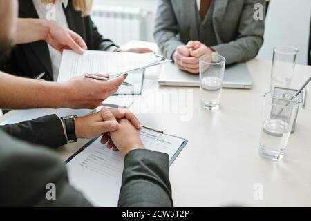 Hands of contemporary business partners over documents sitting by table at break Stock Photo