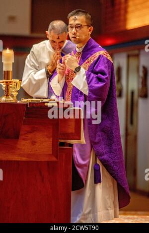Wearing ceremonial robes, a deacon bows his head in prayer as a Vietnamese American priest conducts mass at the altar of a Southern California Catholi Stock Photo