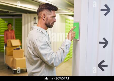 Side view at bearded man using touch pad with green screen while operating self storage unit, copy space