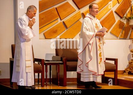 Wearing ceremonial robes, a deacon bows his head in prayer as a priest conducts mass at the altar of a Southern California Catholic church. Stock Photo