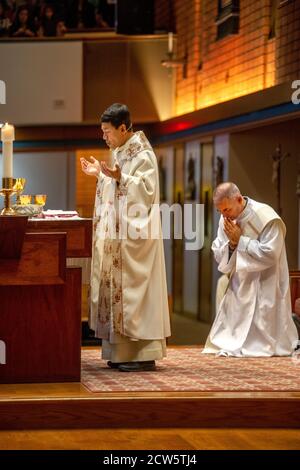Wearing ceremonial robes, a deacon bows his head in prayer as an Asian American priest conducts mass at the altar of a Southern California Catholic ch Stock Photo