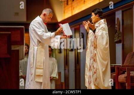 Wearing ceremonial robes, a deacon assists an Asian American priest conducting mass at the altar of a Southern California Catholic church. Stock Photo