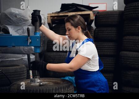 Woman in overalls uses a press to fix a car wheels Stock Photo